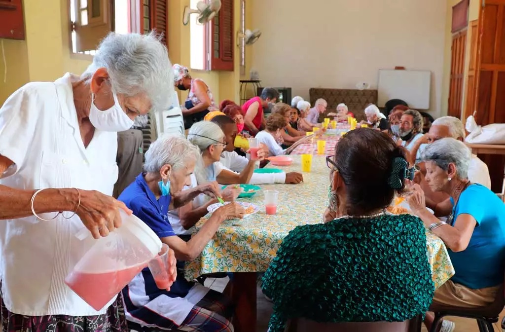 A Caritas Cuba volunteer serves a meal to elderly people at a parish dining room