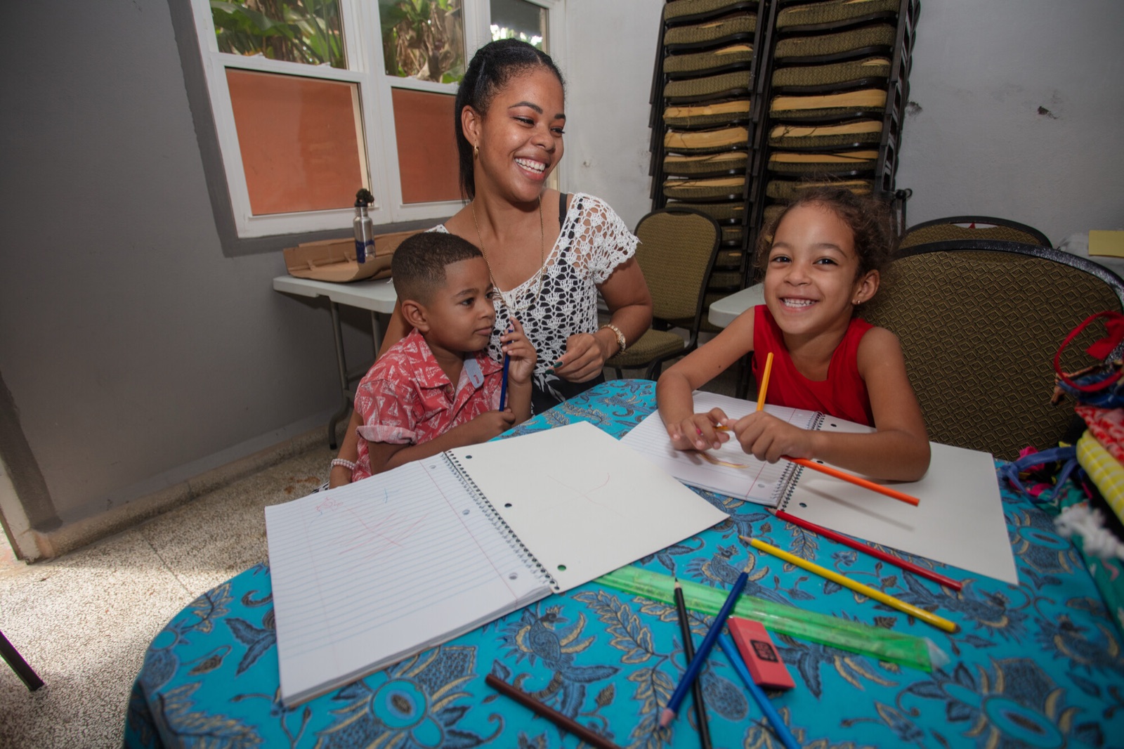A teacher and two children at a table with notebooks and colored pencils in Cuba